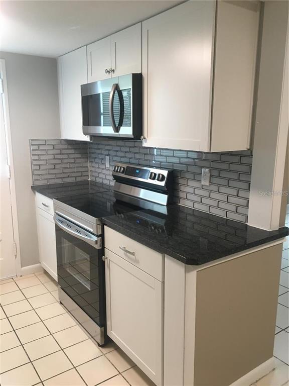 A kitchen features white cabinets, stainless steel appliances, black countertops, and a gray tile backsplash — 2 N FERNWOOD AVENUE UNIT 7, CLEARWATER, FL