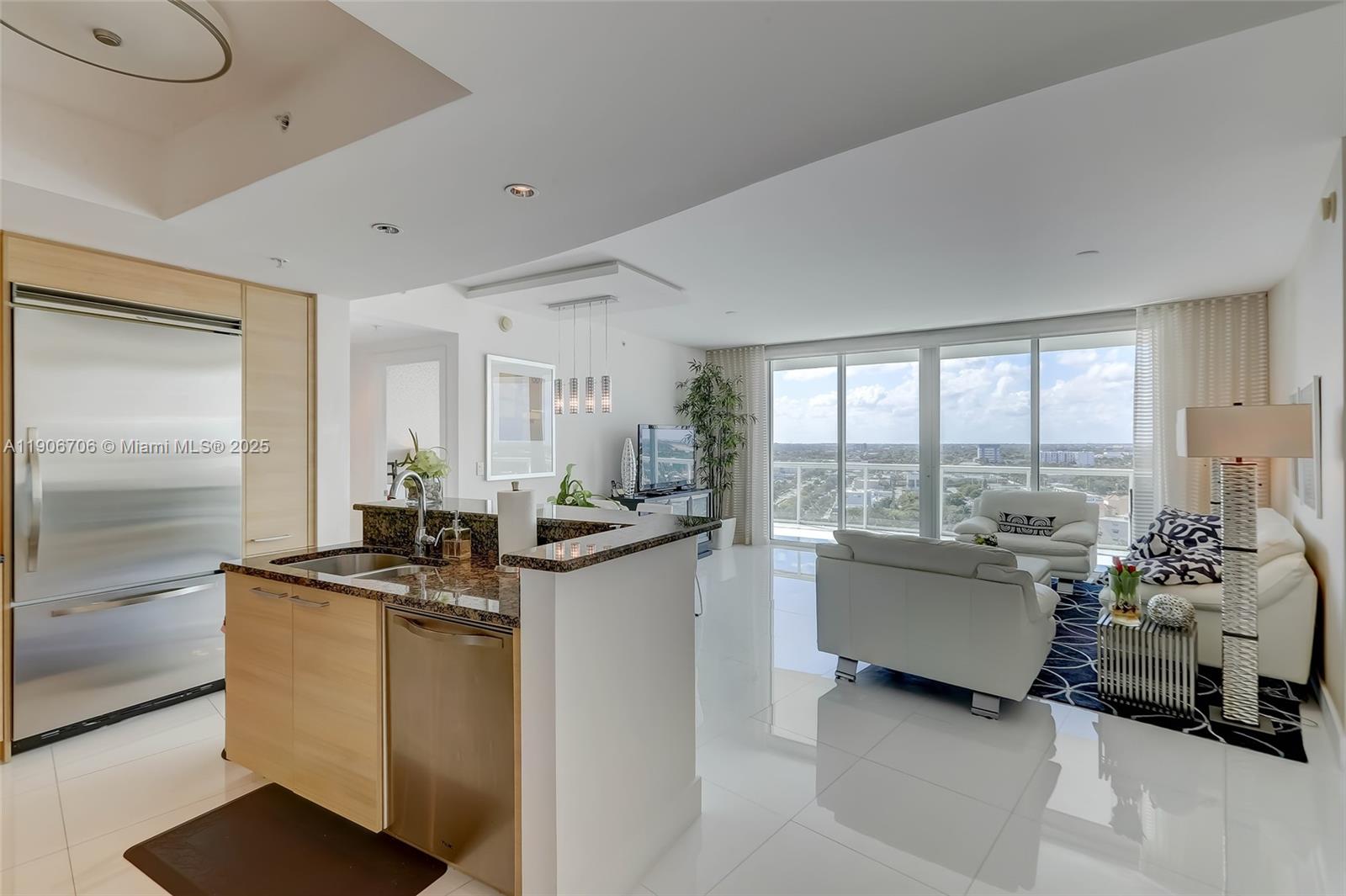 A modern kitchen with stainless steel appliances overlooks a bright living room with floor-to-ceiling windows — 1 N Ocean Blvd # 1411, Pompano Beach FL 33062, POMPANO BEACH, FL