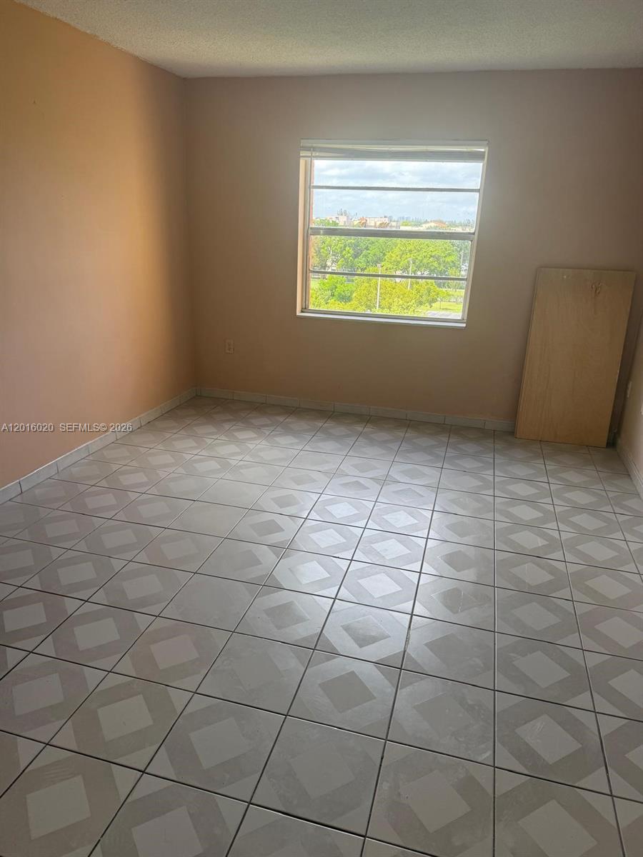 An empty bedroom features light-colored tile flooring, peach-toned walls, and a single window — MIAMI, FL