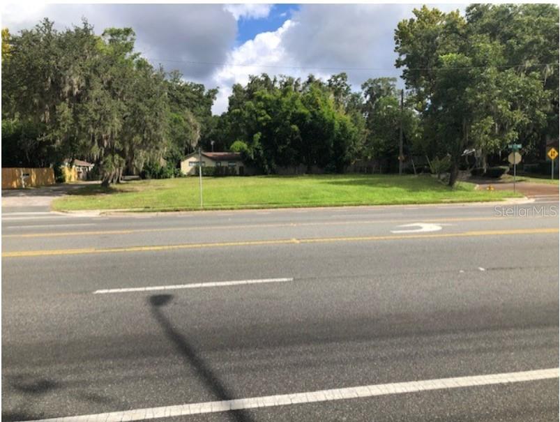 A vacant, grassy lot sits alongside a paved road with trees in the background — 1202 NW 39TH AVENUE, GAINESVILLE, FL