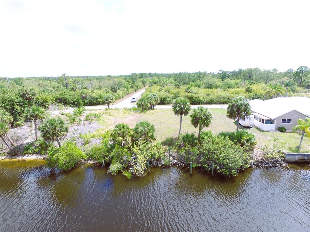 An aerial view shows a waterfront lot with palm trees and vegetation near a road — 13572 WAINWRIGHT DRIVE, PORT CHARLOTTE, FL
