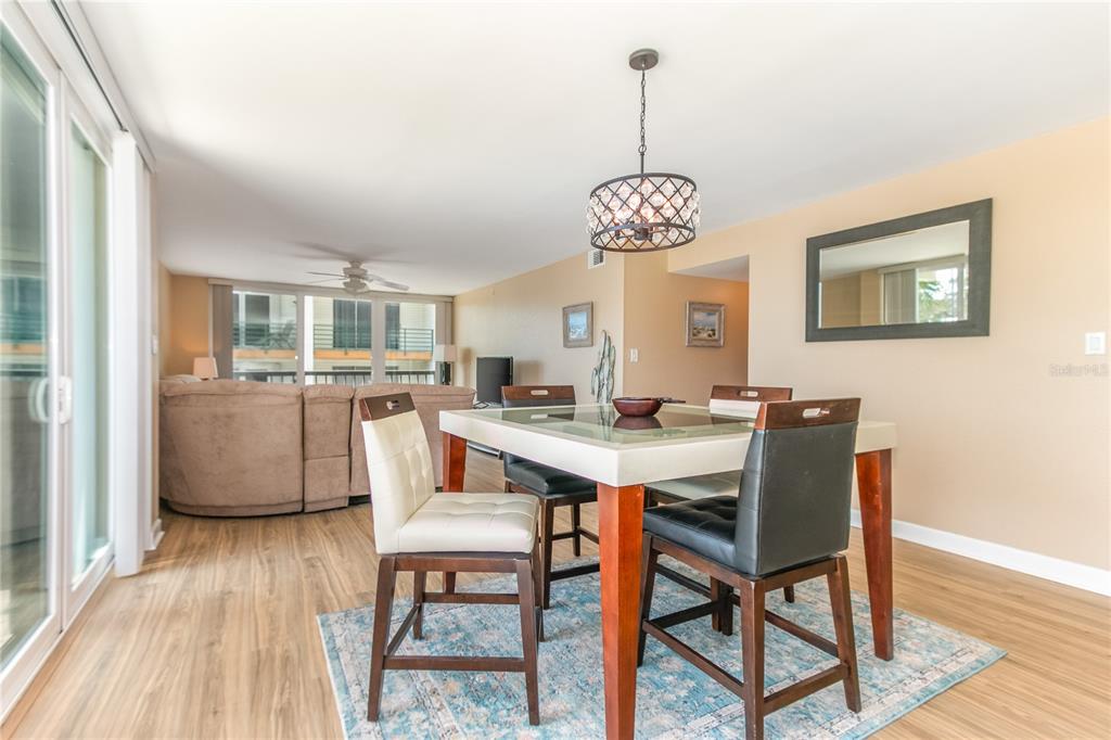 A dining area with a glass-top table, four chairs, and a chandelier on wood flooring — 400 ISLAND WAY UNIT 212, CLEARWATER BEACH, FL