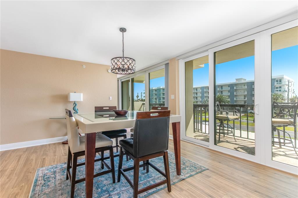 A dining area with a glass-topped table, dark chairs, and sliding doors to a balcony — 400 ISLAND WAY UNIT 212, CLEARWATER BEACH, FL
