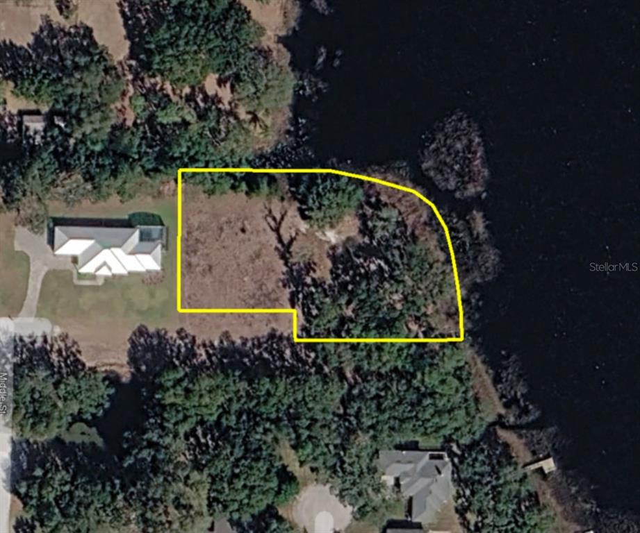 An aerial view shows a vacant, wooded waterfront lot outlined in yellow next to a house — 0 MIDDLE STREET, GROVELAND, FL