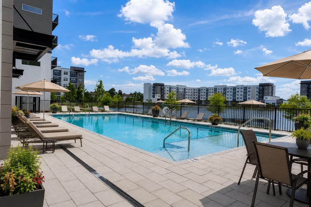 A swimming pool with lounge chairs and umbrellas on a paved deck overlooking a lake — 5579 MILLENIA PARK BOULEVARD UNIT 311, ORLANDO, FL