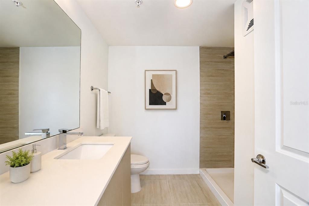 A modern bathroom features a white vanity, a walk-in shower, and neutral tile flooring — 5579 MILLENIA PARK BOULEVARD UNIT 311, ORLANDO, FL