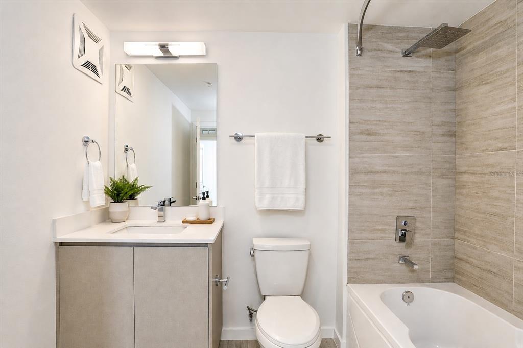 A modern bathroom features a vanity, toilet, and a bathtub with a tiled shower wall — 5579 MILLENIA PARK BOULEVARD UNIT 311, ORLANDO, FL