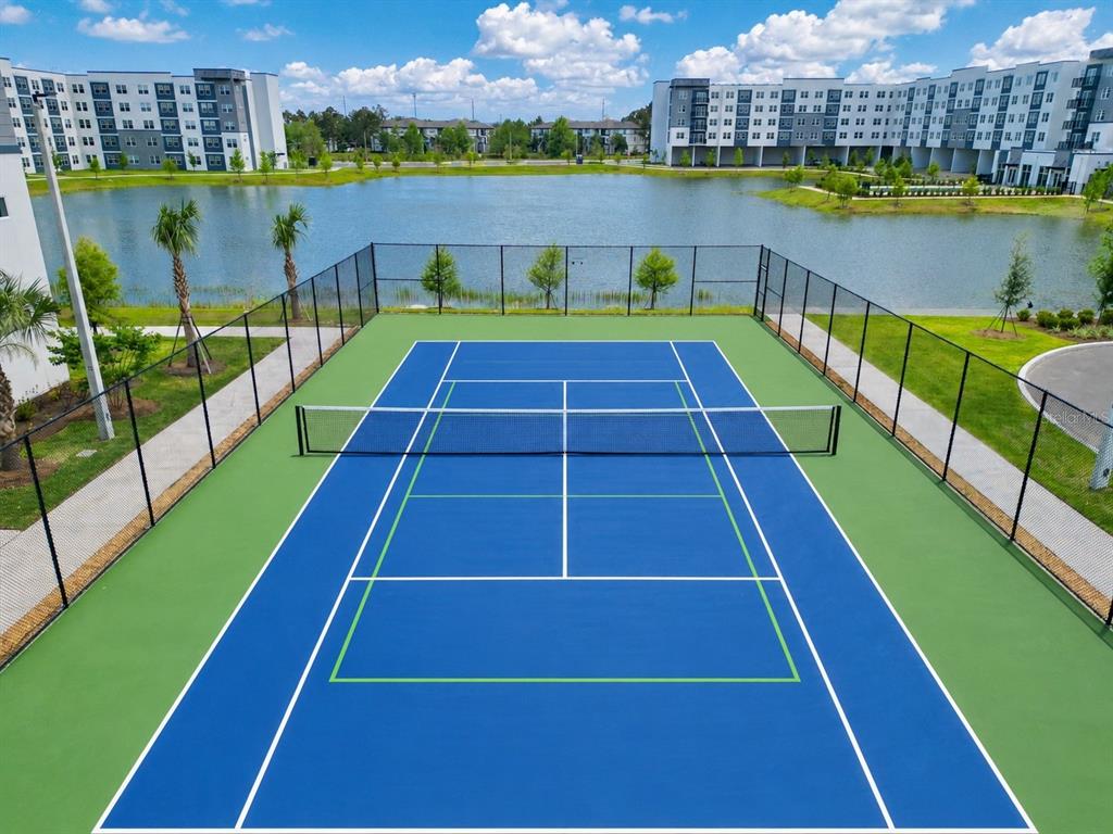 A blue tennis court with a net is situated outdoors next to a large pond — 5579 MILLENIA PARK BOULEVARD UNIT 311, ORLANDO, FL