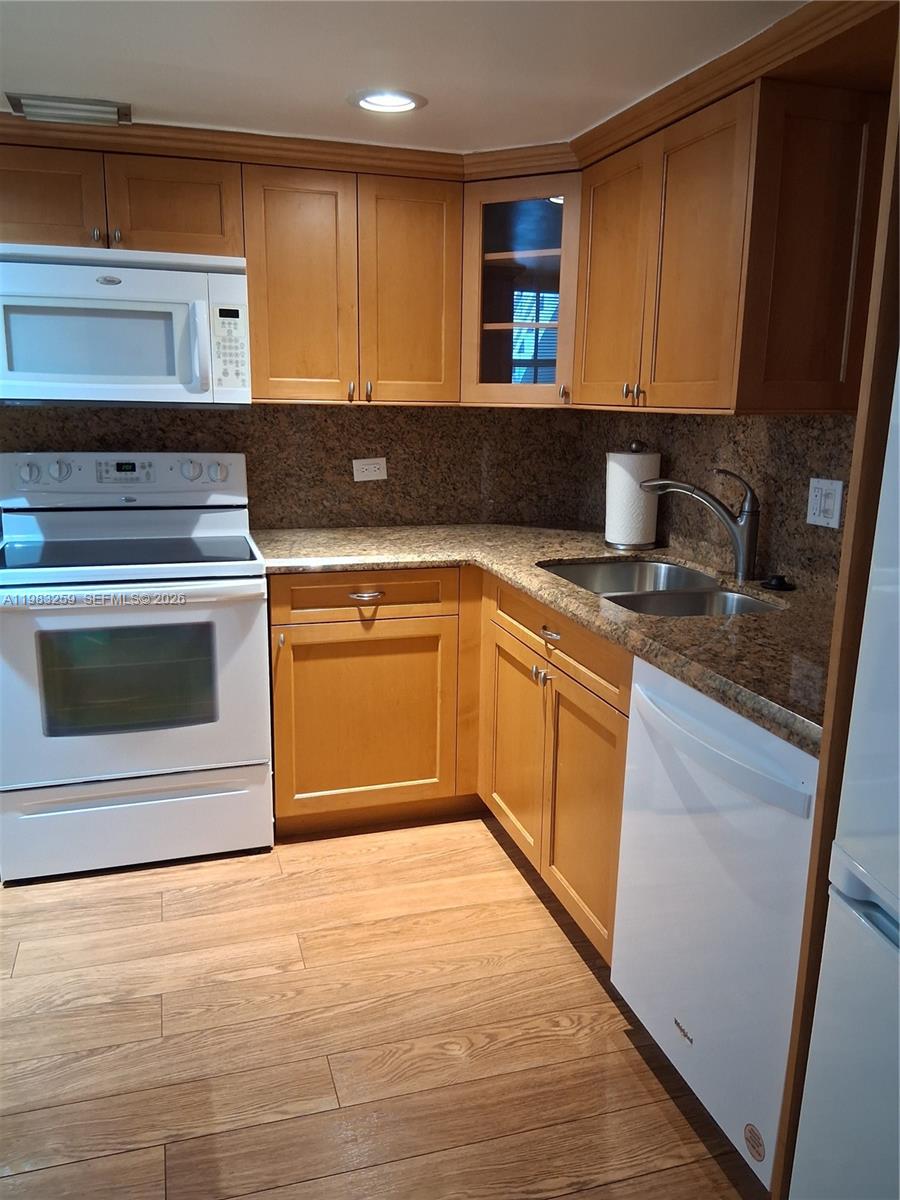 A kitchen features wood cabinets, granite countertops, and white appliances — 7556 Stirling Rd # 123, Davie FL 33024, DAVIE, FL