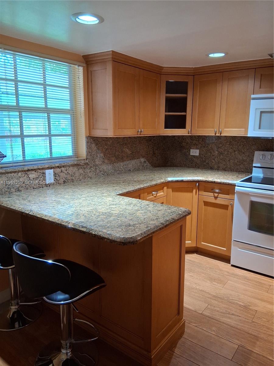 A kitchen features light wood cabinets, granite countertops, and a breakfast bar with stools — 7556 Stirling Rd # 123, Davie FL 33024, DAVIE, FL