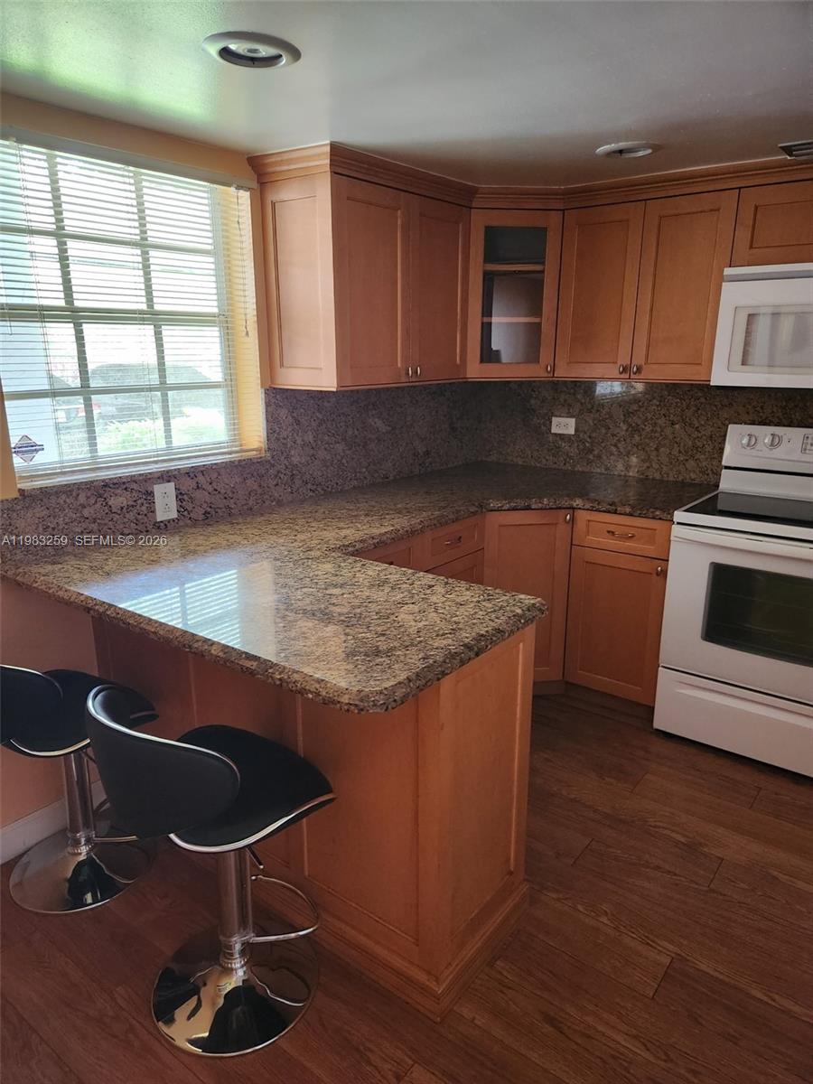 A kitchen features light wood cabinets, granite countertops, and a breakfast bar with two stools — 7556 Stirling Rd # 123, Davie FL 33024, DAVIE, FL