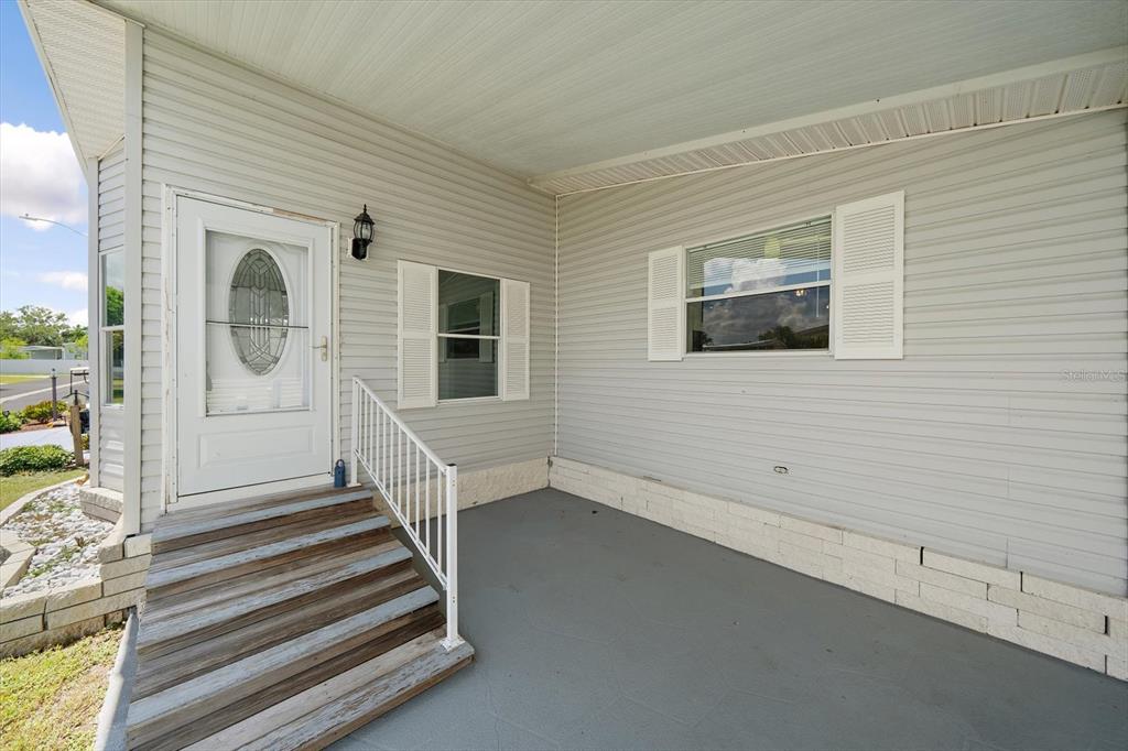 A covered porch with gray siding, a white front door, and wooden steps — 8102 MARIE LANE, ELLENTON, FL