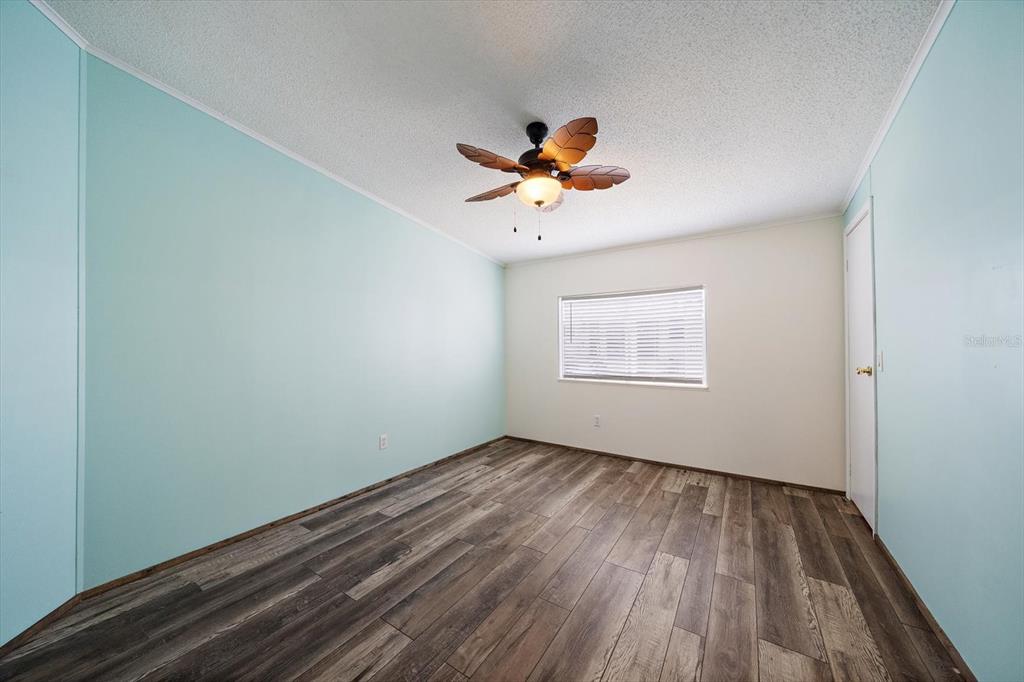 An empty bedroom features light blue walls, wood-look flooring, and a palm-leaf ceiling fan — 8102 MARIE LANE, ELLENTON, FL