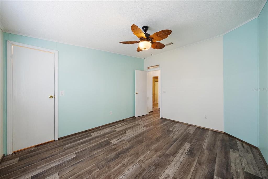 An empty bedroom features light blue and white walls, wood-look flooring, and a ceiling fan — 8102 MARIE LANE, ELLENTON, FL