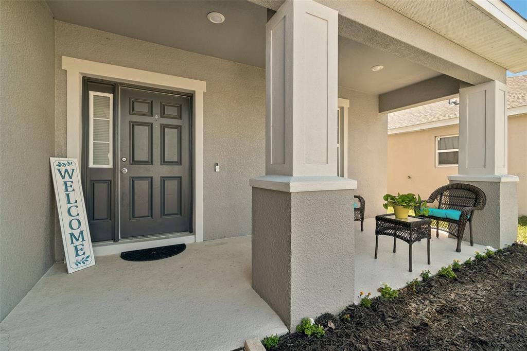A covered front porch features a dark gray door, a welcome sign, and patio furniture — 6396 GARDNER DRIVE, LAKELAND, FL