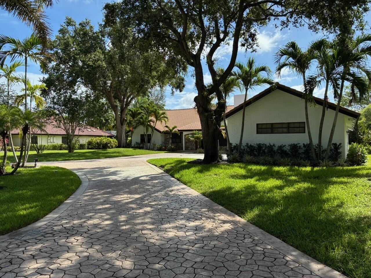 A paved driveway leads to a white house with a tiled roof and palm trees — 7510 E Cypresshead Drive, Parkland FL 33067, PARKLAND, FL