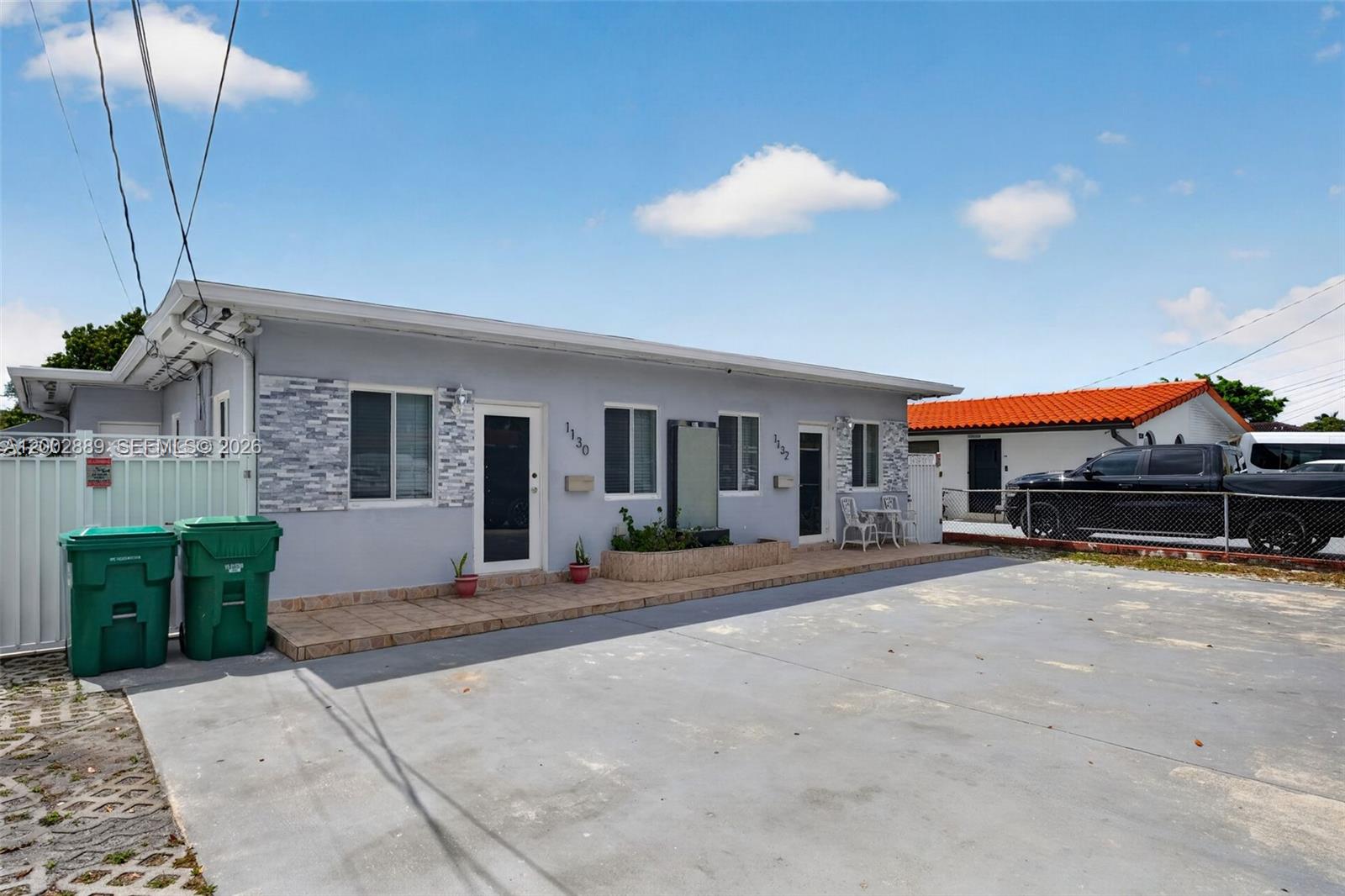 A single-story gray duplex with a paved driveway and two green trash bins outside — 1130-1132 NW 34th Ave, Miami FL 33125, MIAMI, FL