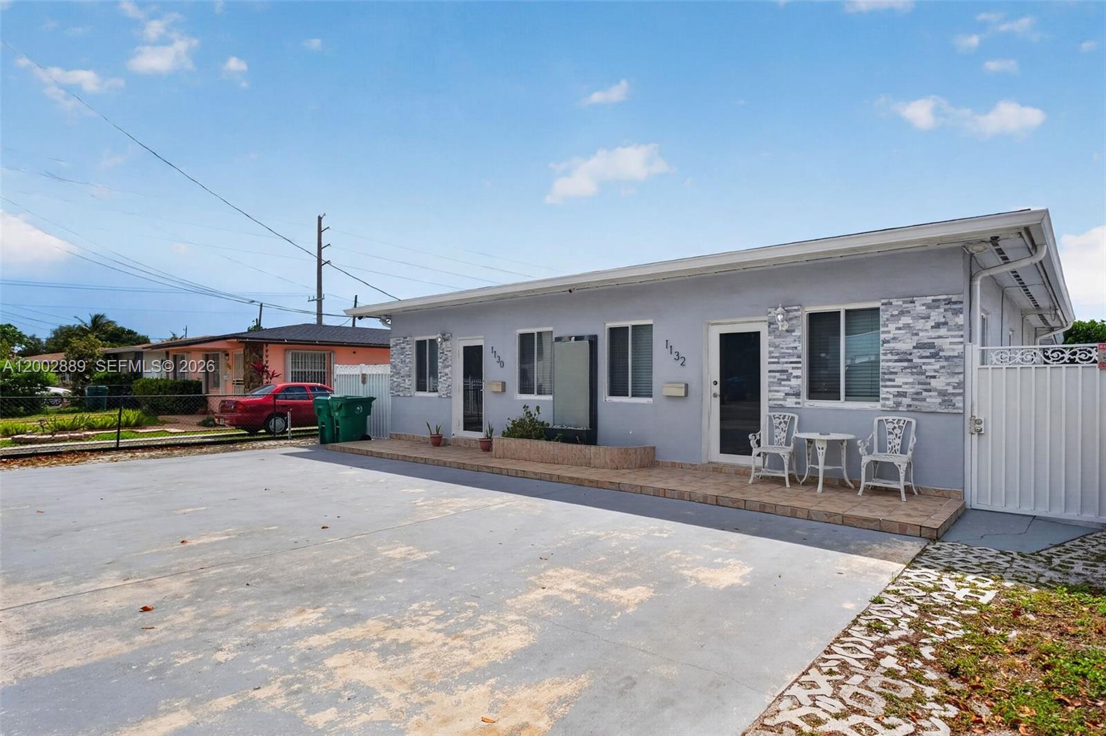 A single-story gray house with a tiled porch, stone accents, and a large concrete driveway — 1130-1132 NW 34th Ave, Miami FL 33125, MIAMI, FL
