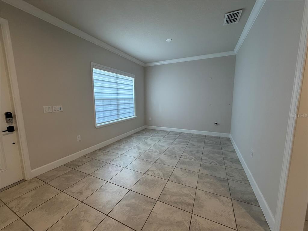 An empty room features light gray walls, crown molding, and large square floor tiles — 2936 SLOUGH CREEK DRIVE, KISSIMMEE, FL