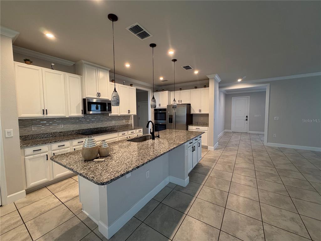 A kitchen features white cabinets, granite countertops, a central island, and tile flooring — 2936 SLOUGH CREEK DRIVE, KISSIMMEE, FL