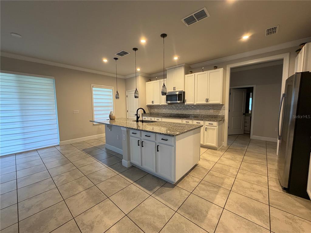 A kitchen features white cabinets, granite countertops, a central island, and light-colored tile flooring — 2936 SLOUGH CREEK DRIVE, KISSIMMEE, FL
