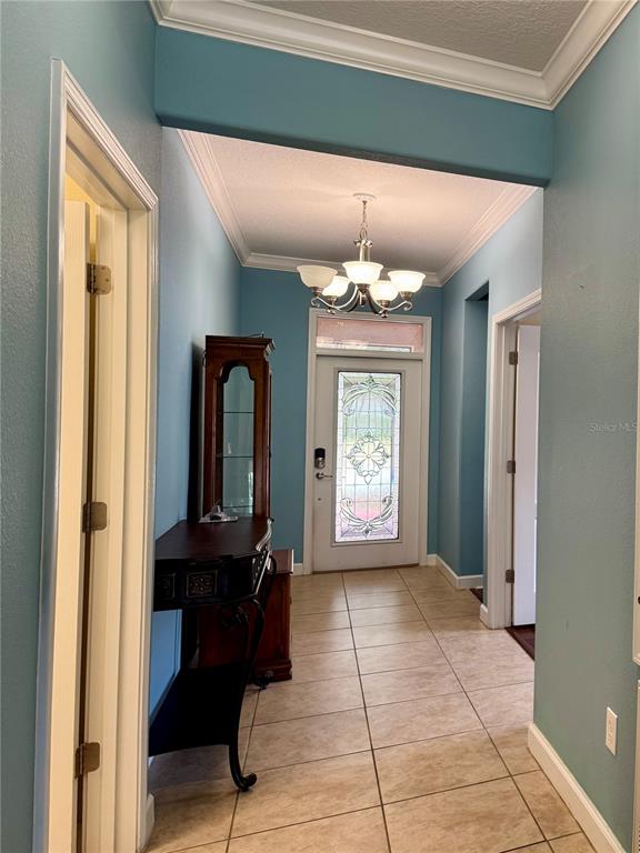 A tiled entryway features a chandelier, a wooden display cabinet, and a glass-paneled front door — 4056 SERENA LANE, CLERMONT, FL