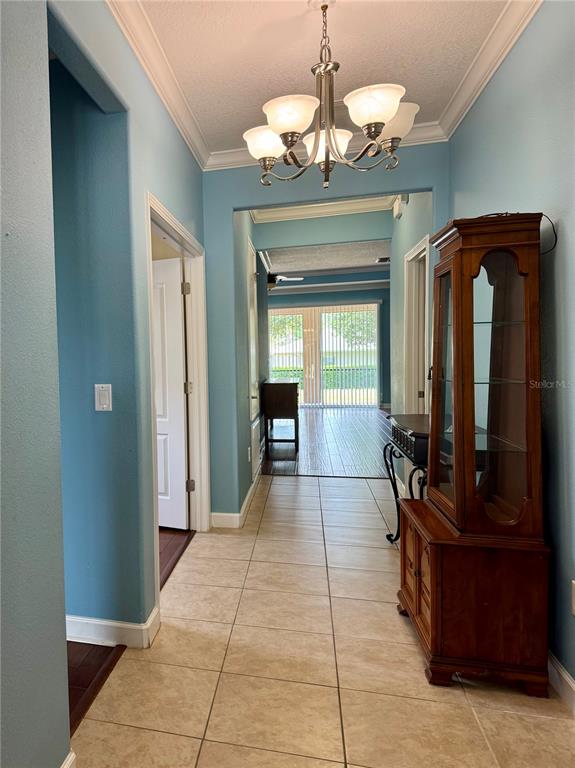 A tiled hallway leads to a living area with sliding glass doors and a chandelier — 4056 SERENA LANE, CLERMONT, FL
