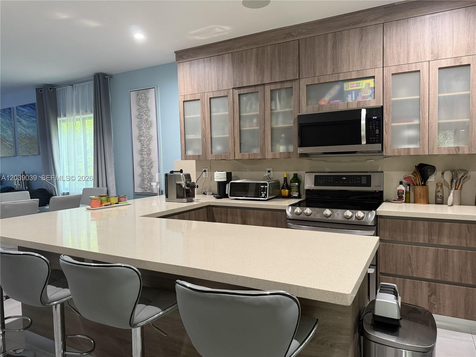 A modern kitchen features wood-grain cabinets, light quartz countertops, and a breakfast bar with stools — KEY LARGO, FL