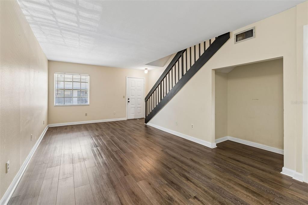 A living room with wood-look flooring, a staircase with dark railings, and a galley kitchen — 4839 MCELROY UNIT F206, TAMPA, FL
