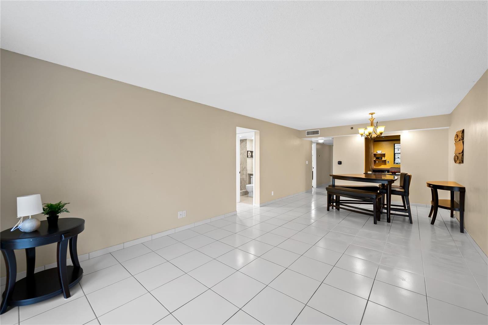 A spacious room features white tile flooring, beige walls, a dining set, and a side table — 3300 W Rolling Hills Circle # 610, Davie FL 33328, DAVIE, FL