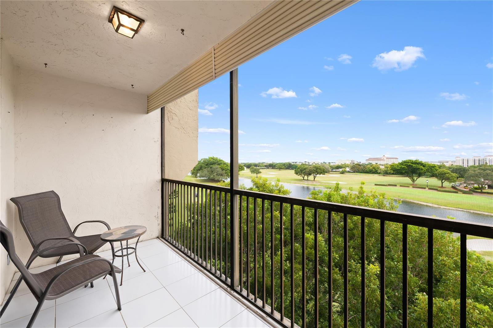 A balcony with white tile flooring, two chairs, a small table, and a golf course view — 3300 W Rolling Hills Circle # 610, Davie FL 33328, DAVIE, FL