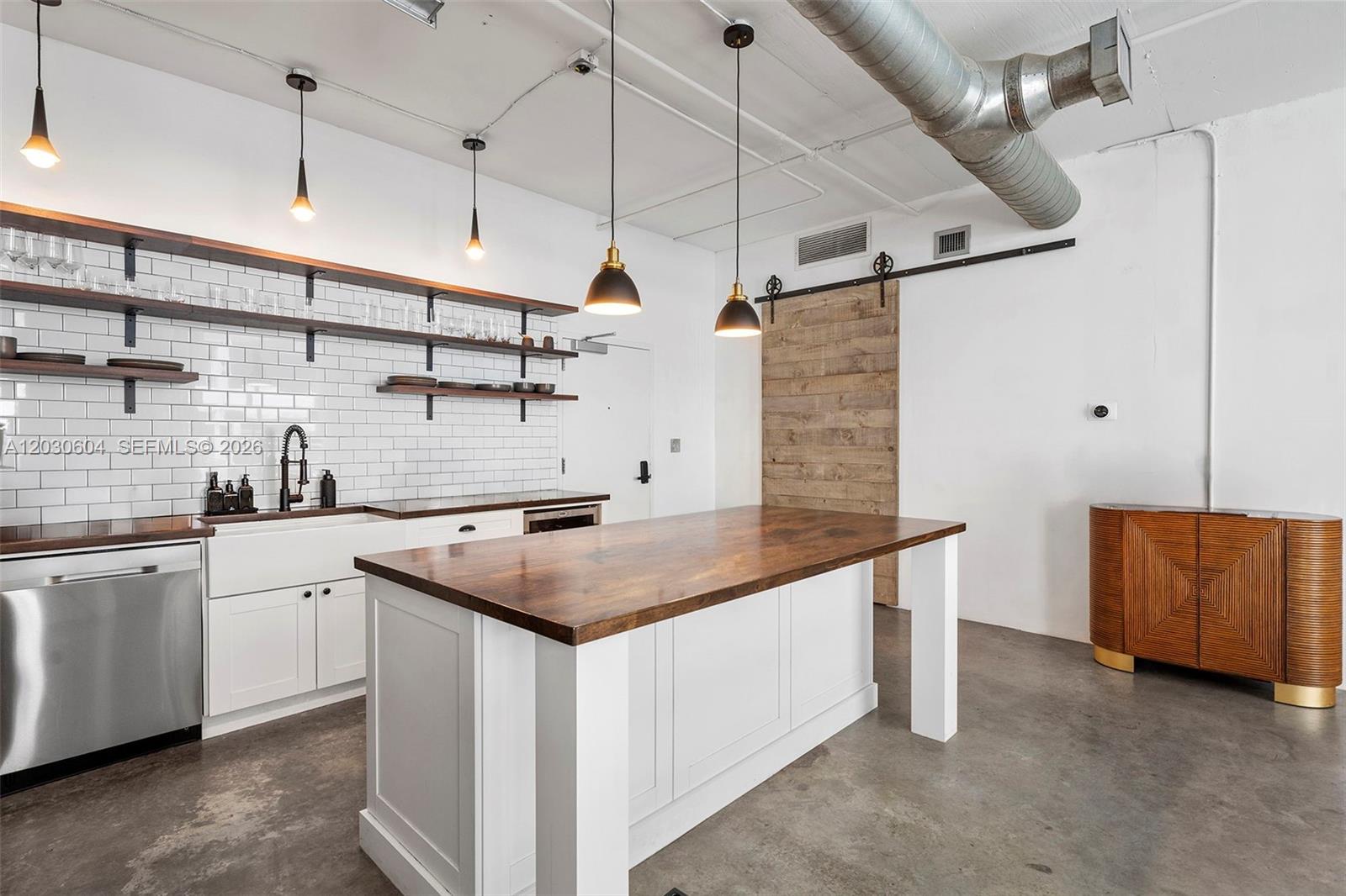 A modern kitchen features white cabinets, open wood shelving, a central island, and concrete floors — 444 NE 30th St # 402, Miami FL 33137, MIAMI, FL