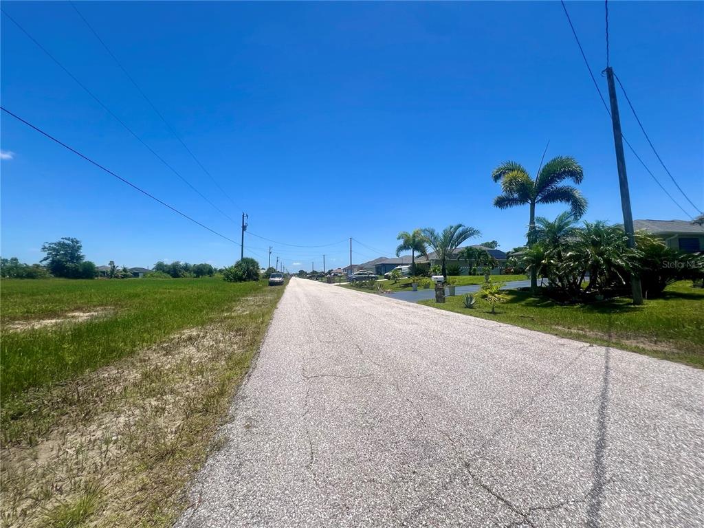 A paved road stretches through a residential neighborhood with palm trees and grassy lots — 2229 NW 9TH TERRACE, CAPE CORAL, FL