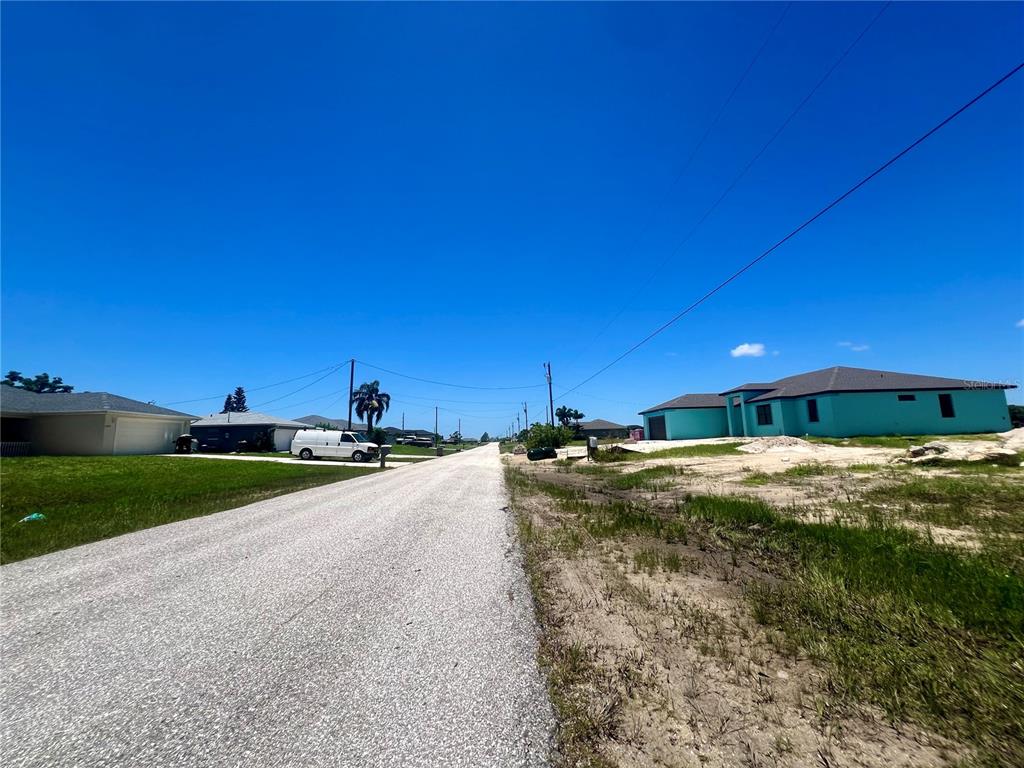 A paved road runs between residential houses under a clear blue sky — 2229 NW 9TH TERRACE, CAPE CORAL, FL