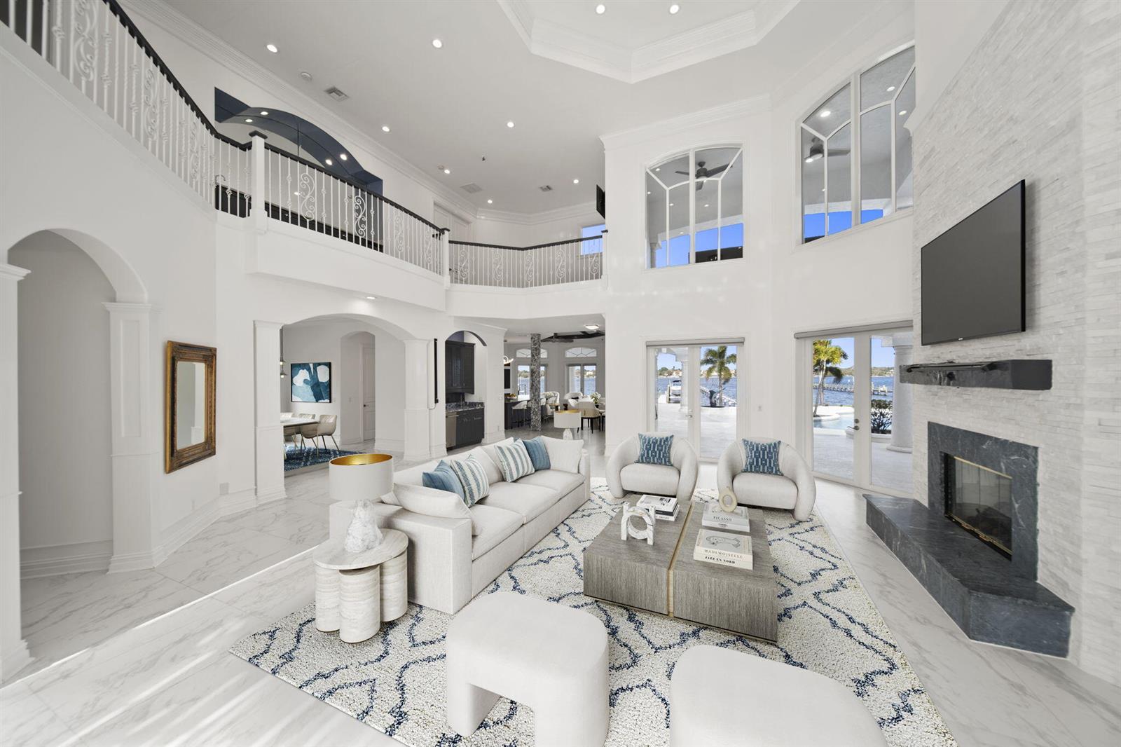 A bright, two-story living room features a stone fireplace, white furniture, and large windows — 1735 SE St Lucie Boulevard, Stuart FL 34996, STUART, FL