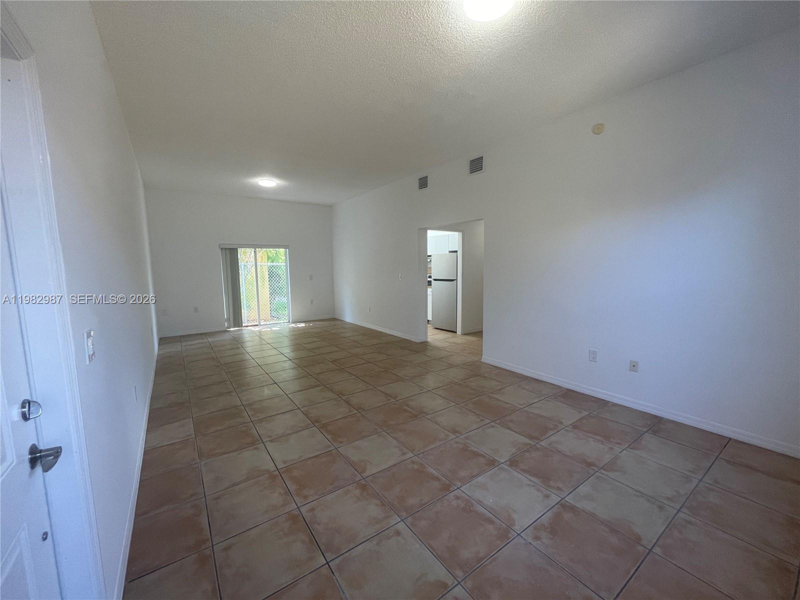An empty room features white walls, tan tile flooring, and a sliding glass door — 3421 SW 25th St # 01, Miami FL 33133, MIAMI, FL