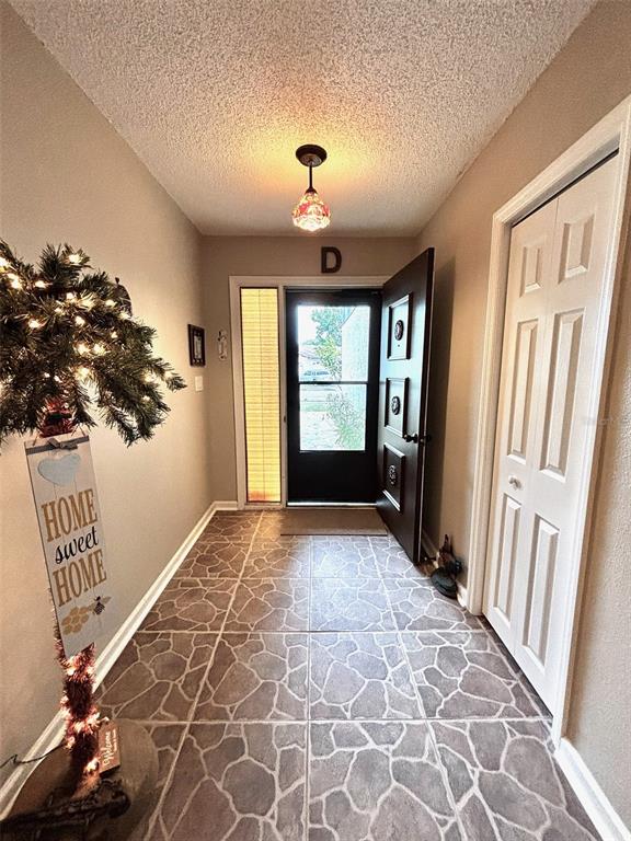 An entryway features stone-patterned tile flooring, a decorative light fixture, and a dark front door — 8034 BADGER LANE, NEW PORT RICHEY, FL
