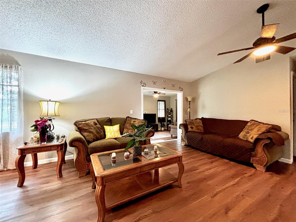 A living room features two brown sofas, a glass-topped coffee table, and wood-look flooring — 8034 BADGER LANE, NEW PORT RICHEY, FL