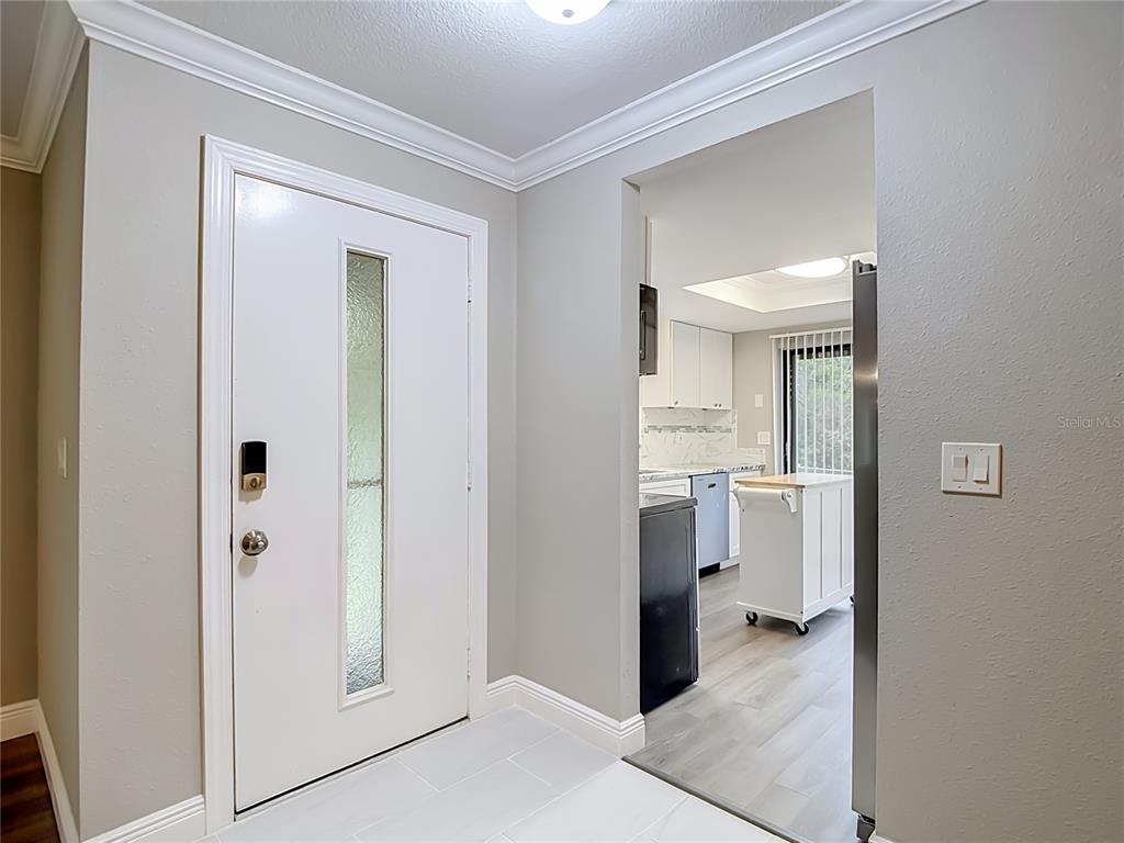 A white front door opens into a tiled entryway looking toward a kitchen with cabinets — 12308 EAGLESWOOD DRIVE UNIT D, HUDSON, FL