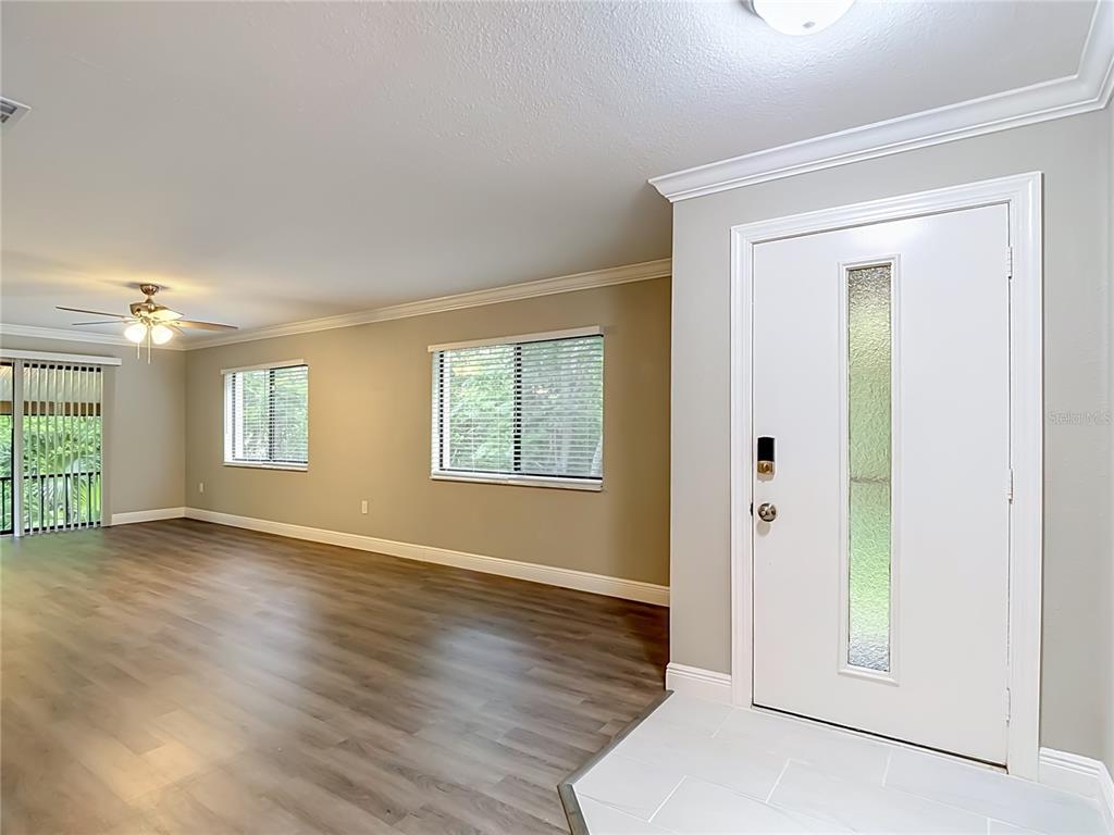 An entryway with white tile flooring leads into a living room with wood-look flooring — 12308 EAGLESWOOD DRIVE UNIT D, HUDSON, FL