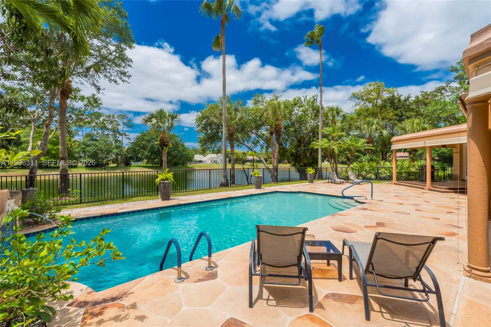 A swimming pool with lounge chairs on a stone patio overlooks a lake and trees — 5328 E Leitner Dr, Coral Springs FL 33067, CORAL SPRINGS, FL