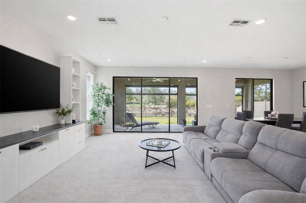 A living room with a large television, grey sectional sofa, and sliding glass patio doors — 4547 SAN MARTINO DRIVE, WESLEY CHAPEL, FL