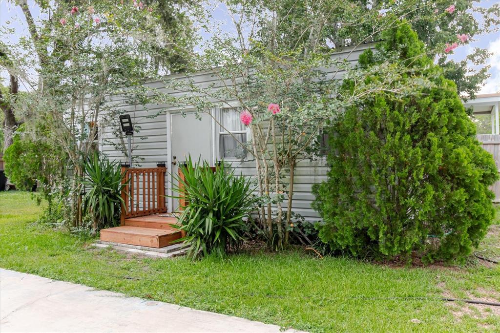 A small, light-gray mobile home features a wooden front porch and lush landscaping — 9916 E GULF TO LAKE HIGHWAY, INVERNESS, FL
