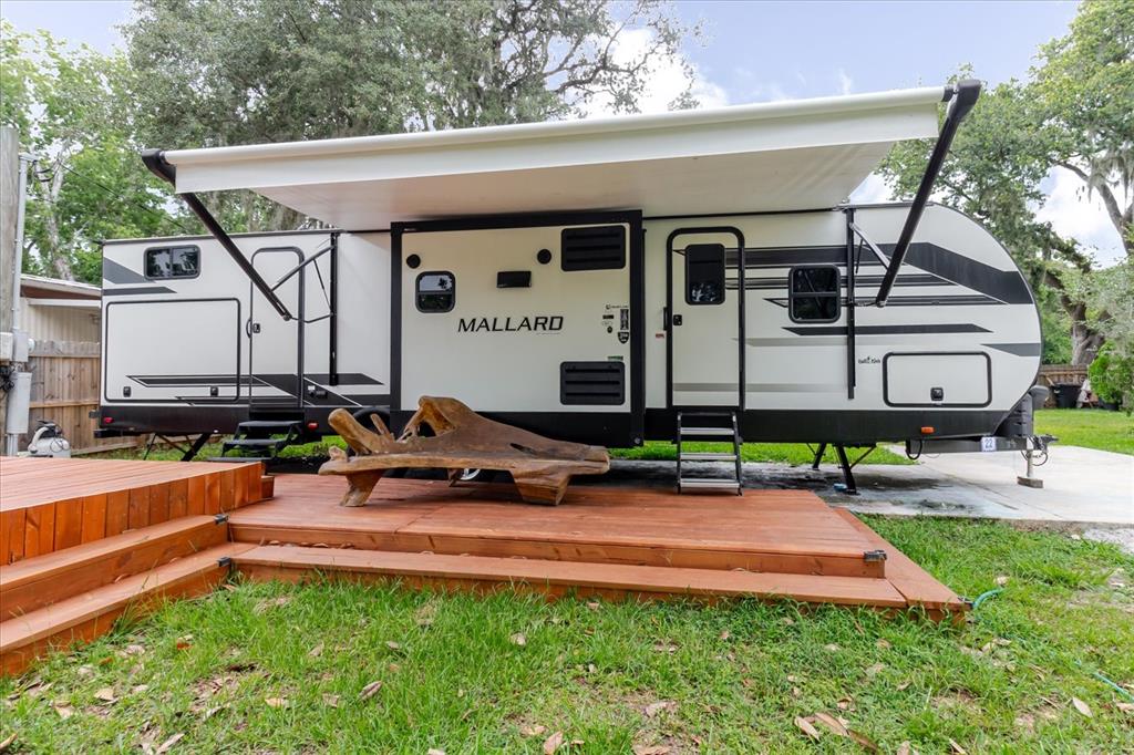 A Mallard travel trailer is parked next to a wooden deck with a rustic bench — 9916 E GULF TO LAKE HIGHWAY, INVERNESS, FL