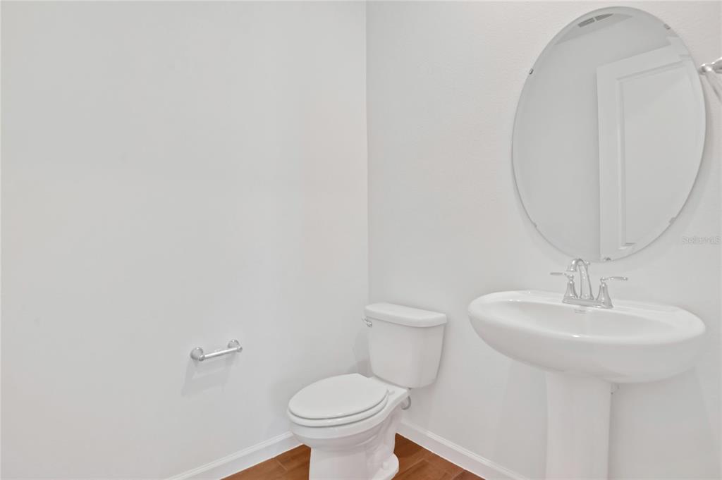 A bathroom features a pedestal sink, an oval mirror, and a toilet on wood flooring — 734 LAKE DELL AVENUE, DUNDEE, FL