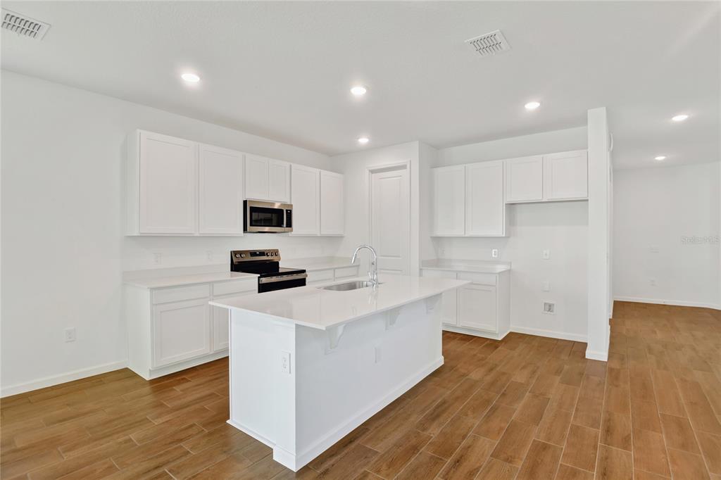 A modern kitchen features white cabinetry, a central island, and wood-look tile flooring — 734 LAKE DELL AVENUE, DUNDEE, FL