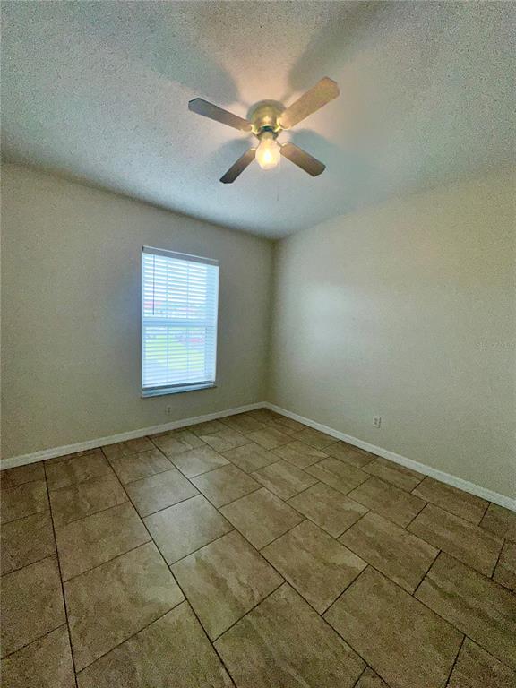 An empty bedroom features beige walls, tile flooring, and a ceiling fan with a light — 2850 OSPREY COVE PLACE UNIT 201, KISSIMMEE, FL