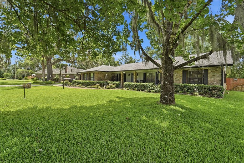 A single-story brick house with a large lawn and mature trees under a blue sky — 386 LAKE CHARLES ROAD, DELAND, FL