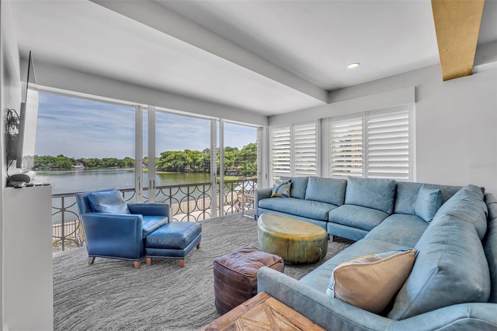 A living room features a blue sectional sofa, matching armchair, and large windows overlooking water — 311 E MORSE BOULEVARD UNIT 1-3, WINTER PARK, FL