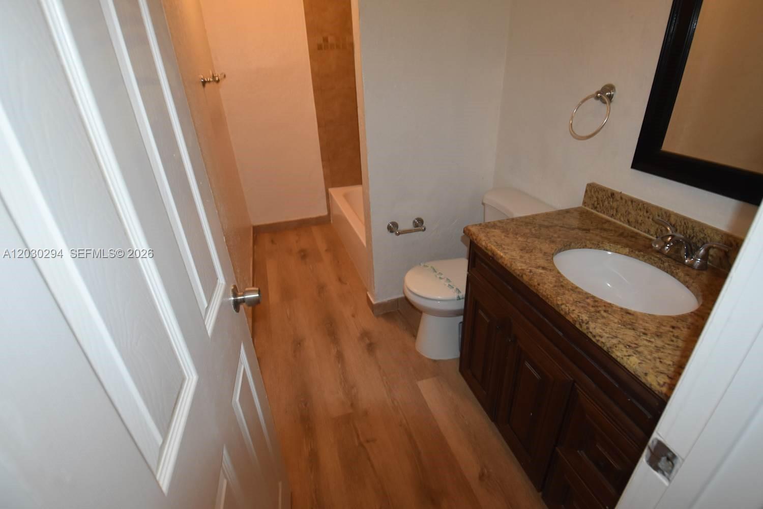 A bathroom features a wood-look floor, a granite vanity, and a tub-shower combination — SUNRISE, FL